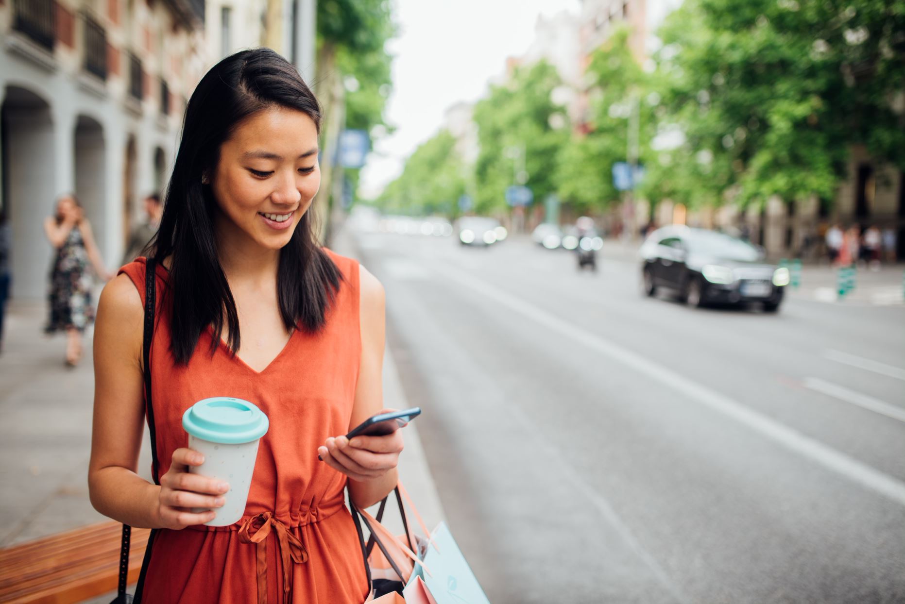 person with a cup of coffee walking on the street and checking her phone